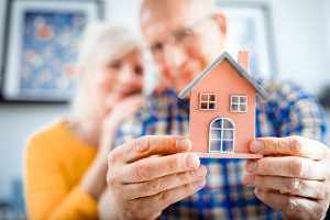 New house concept, happy senior couple holding small home model